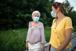 Mother and daughter with protective face mask, walking down street and talking