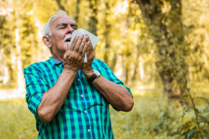 Older man preparing to sneeze while standing in a park or forest