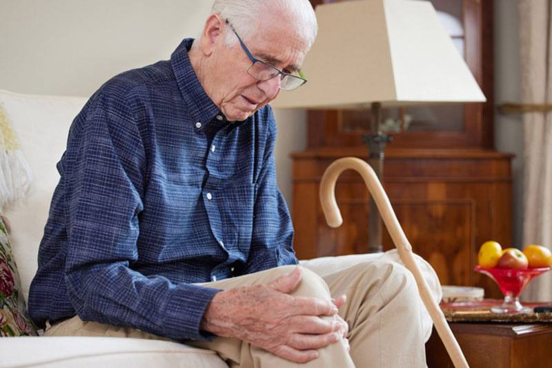 An older man clutches his knee and thinks about the questions he will ask his doctor that are essential to know before a hip or knee replacement.